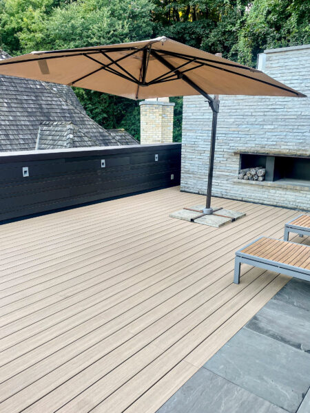Spacious outdoor patio with lounge chairs, a large umbrella, and surrounded by trees under a clear sky.