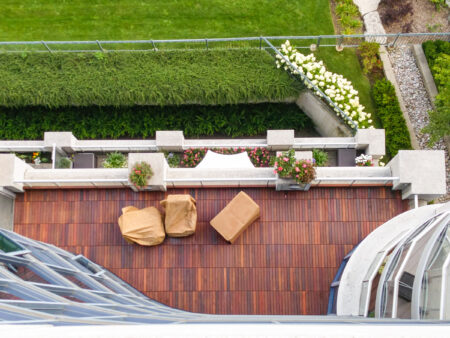Aerial view of an IPE wooden balcony with two covered chairs, a table, and potted plants overlooking a green lawn.