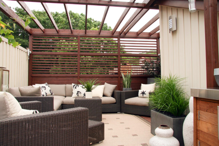 Outdoor patio with wicker furniture, beige cushions, potted plants, and a wooden pergola with slatted privacy screen.