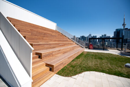 Wide wooden bleacher-style seating on a rooftop with city skyline and blue sky in the background.