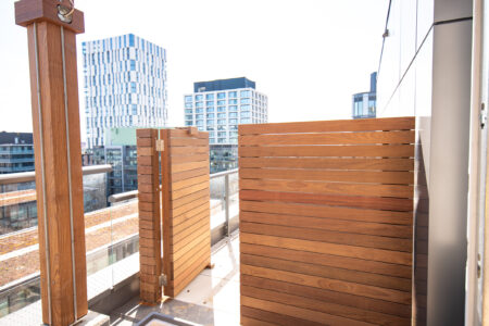 A modern balcony with wooden privacy screens and a view of contemporary buildings in the background.