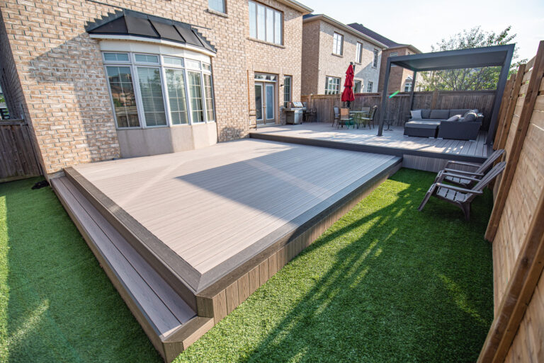 Modern backyard with raised composite deck, outdoor seating area under a pergola, and artificial grass lawn.