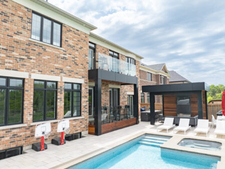 A modern backyard with a pool, hot tub, lounge chairs, patio seating area, and dining table with a red umbrella.