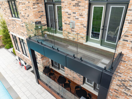 A modern brick building with a glass balcony above a patio area with tables and chairs beside a pool.